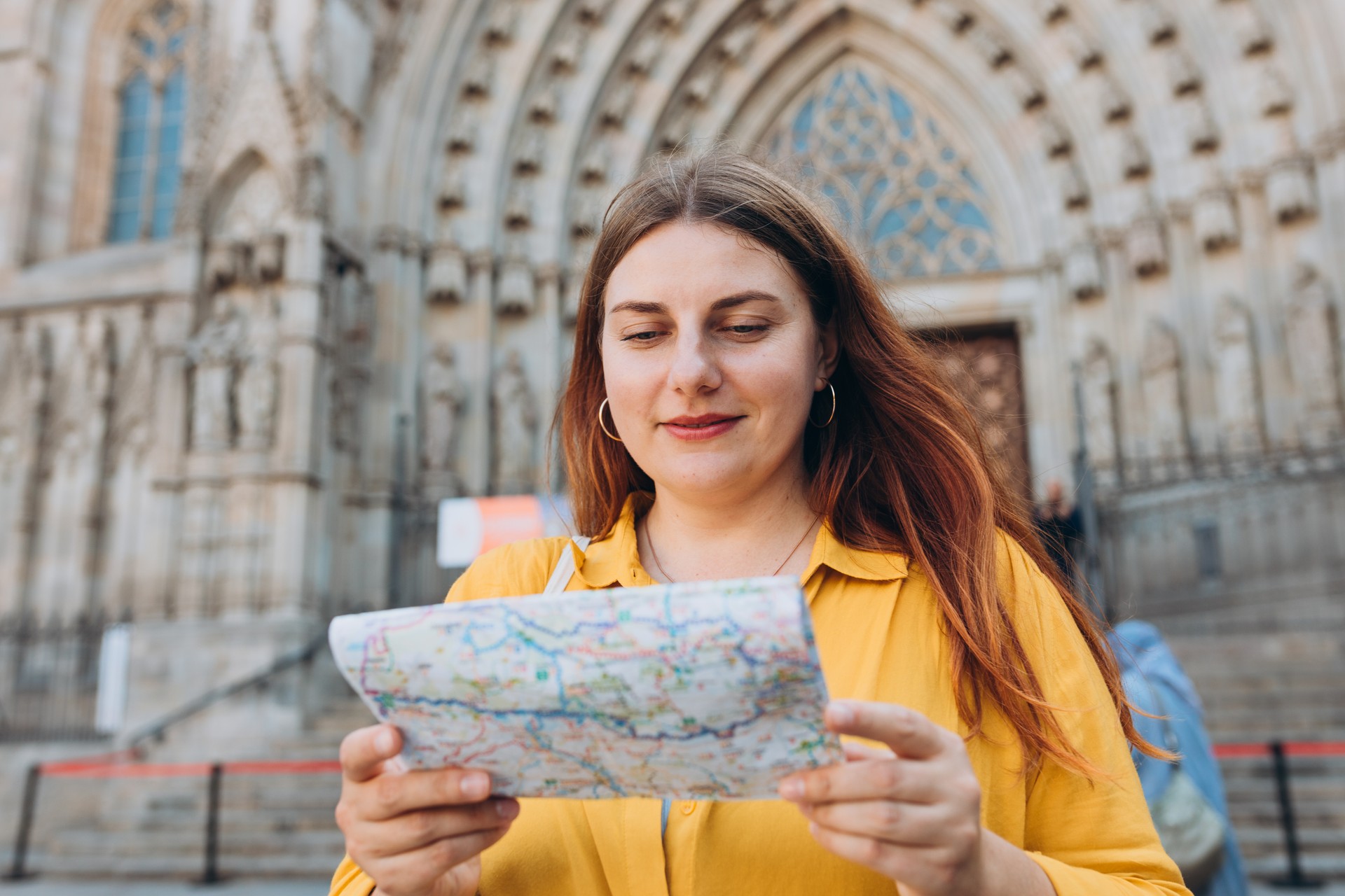 Young woman tourist with paper map standing in front of the famous saint Eulalia church in Barcelona. Concept of travel, tourism and vacation in city. Cathedral of Barcelona